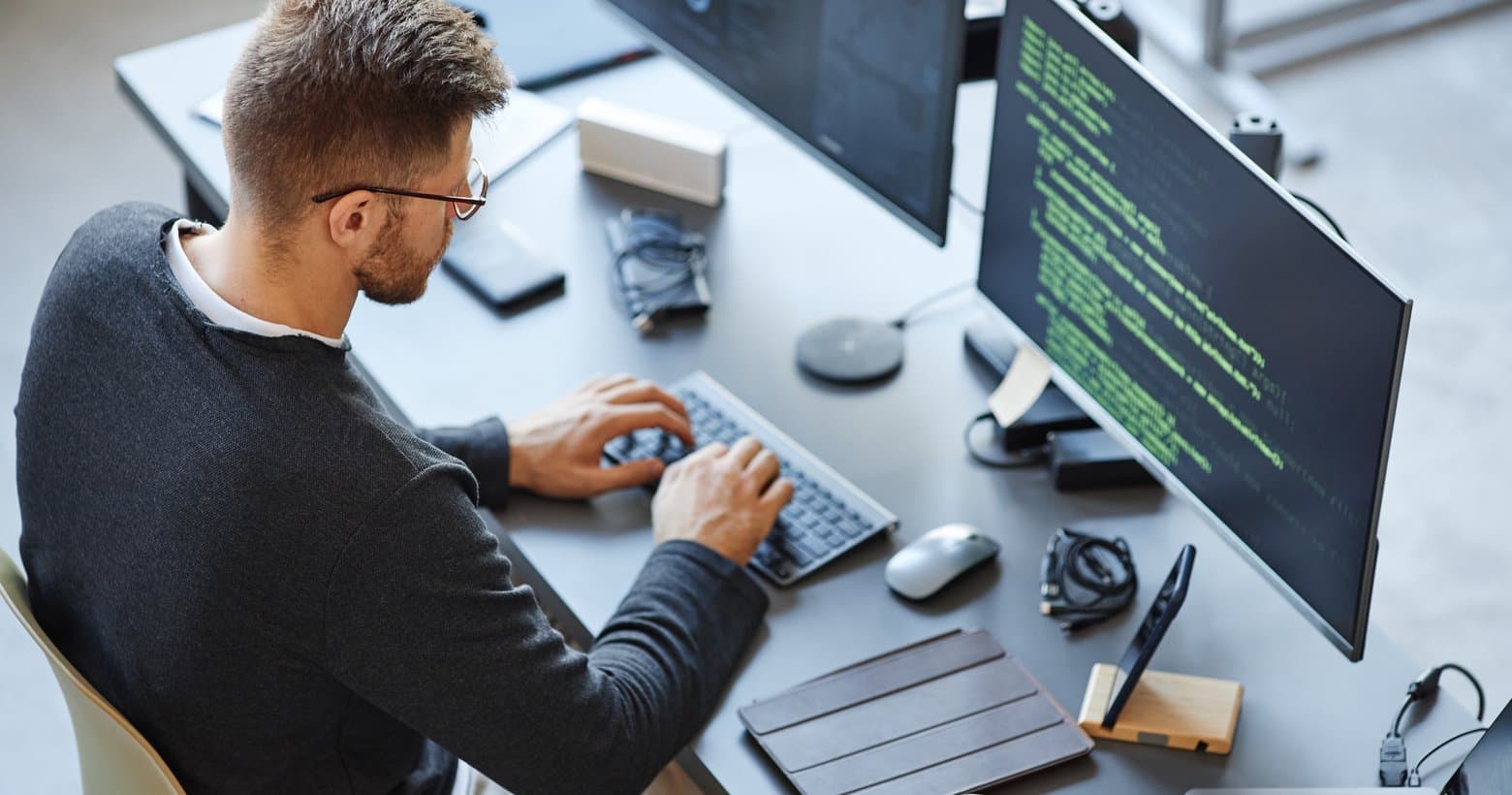 A developer at a desk typing on a keyboard, with source code on the monitor beside them